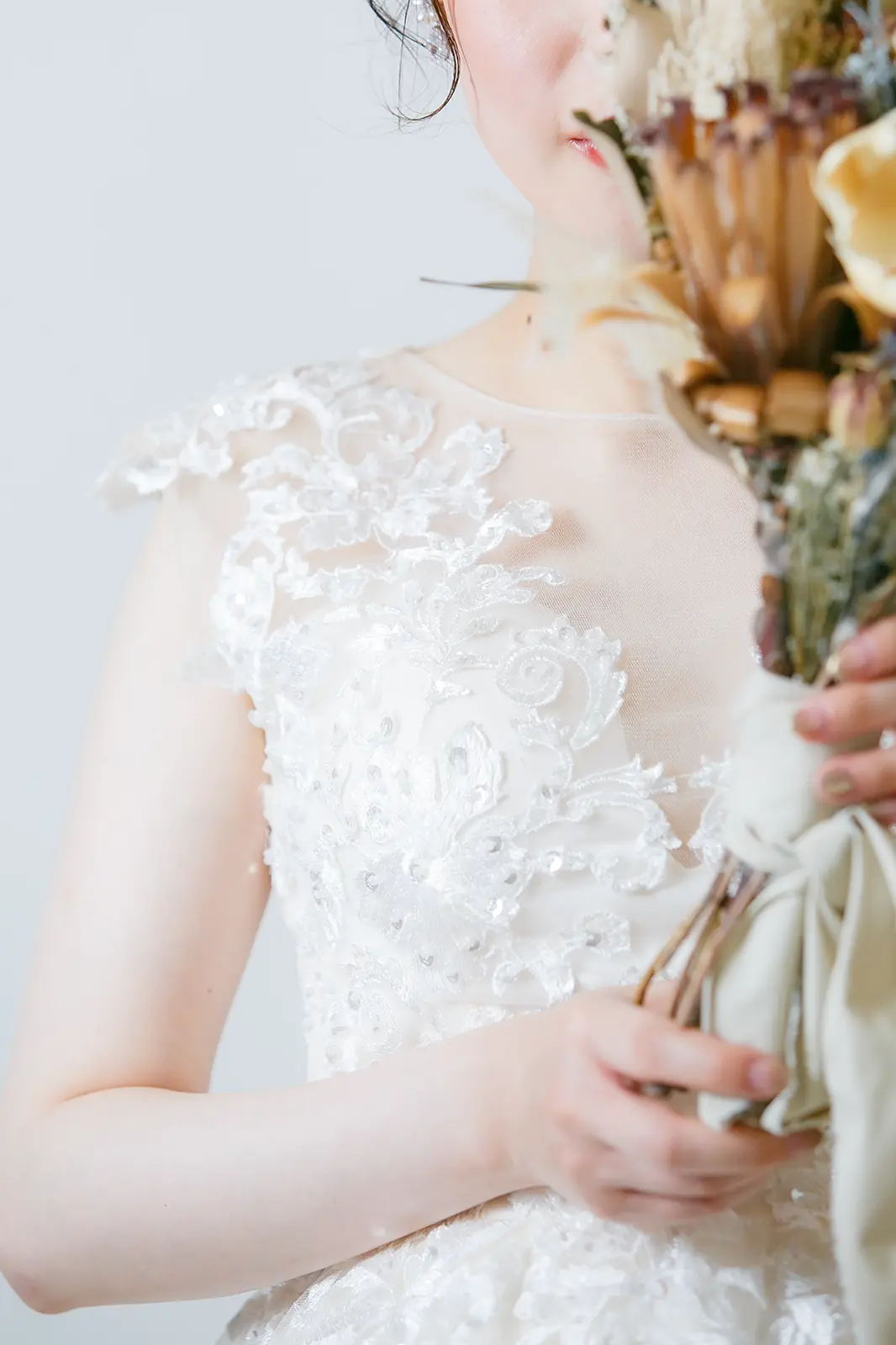 繊細な刺繍が施されたホワイトのウェディングドレスを着用し、ドライフラワーブーケを持つ花嫁。ブルベ肌の透明感を引き立てる、フォトジェリッシュの上質なドレススタイル。