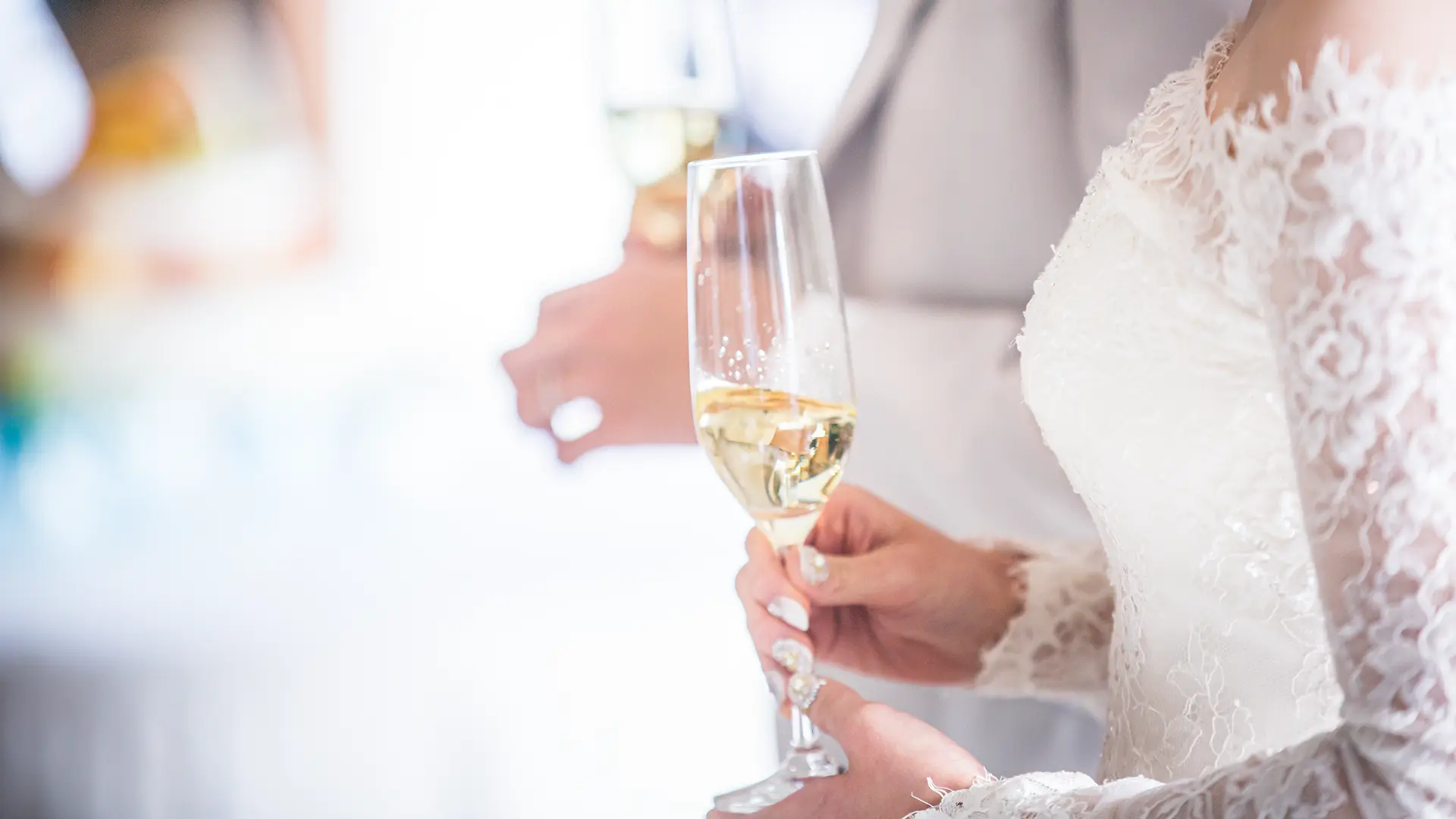 ウェディングドレス姿の花嫁がシャンパングラスを手に持ち、乾杯をしている手元のアップ。幸せに満ちた結婚式・会食の祝福の瞬間。