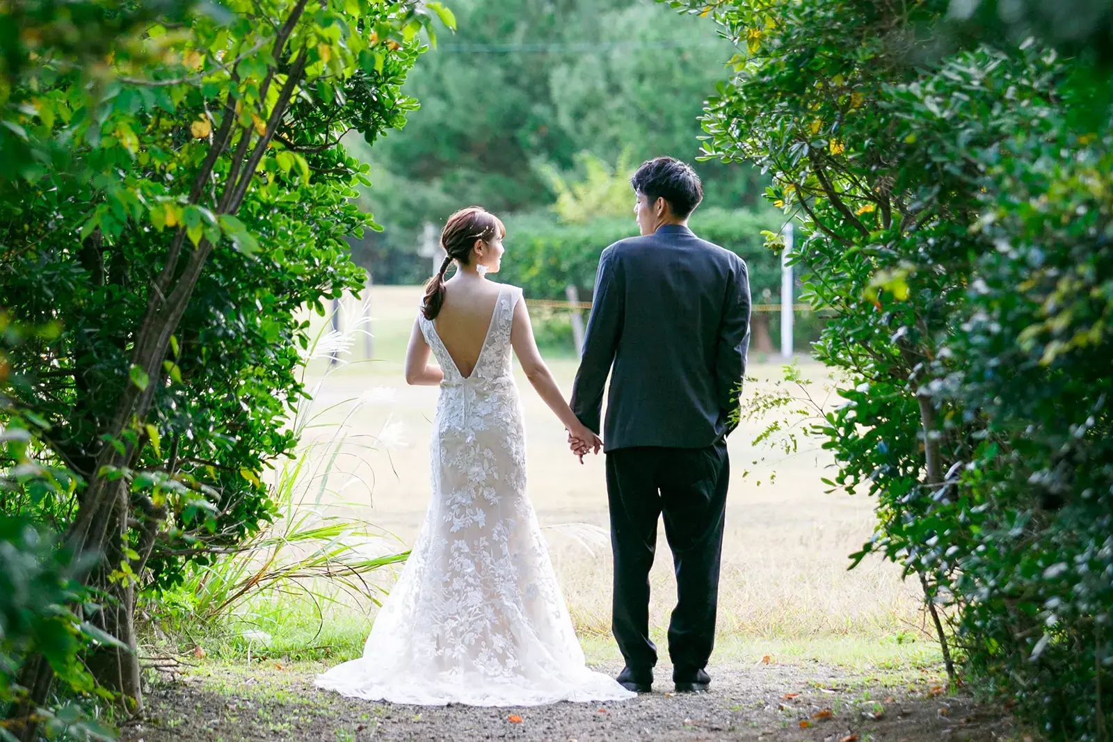 県民海浜公園の緑の小道で手をつないで歩く新郎新婦のフォトウェディング