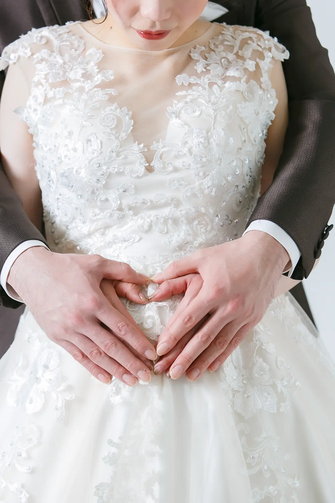 ウェディングドレス姿のプレママが、お腹の上でパートナーと手でハートマークを作っているマタニティフォト。フォトジェリッシュによる優しい雰囲気の前撮り。