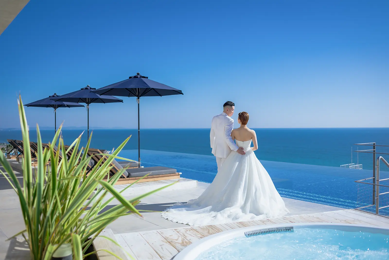 大磯プリンスホテルのインフィニティプールを背景に、青い海と空に包まれて立つ新郎新婦のフォトウェディング。洗練された湘南リゾートの雰囲気。