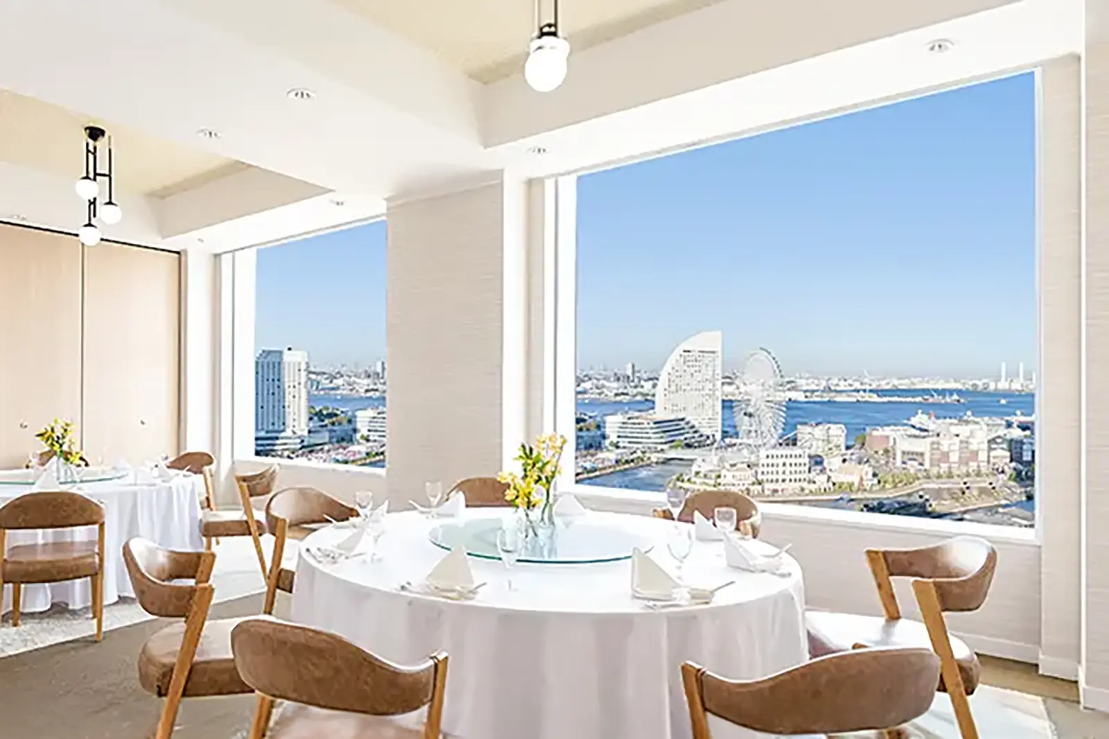 横浜・東天紅みなとみらい店の会食会場。大きな窓からみなとみらいの海と観覧車が一望でき、明るく開放的な雰囲気の中で円卓が並ぶウェディングパーティーの様子。