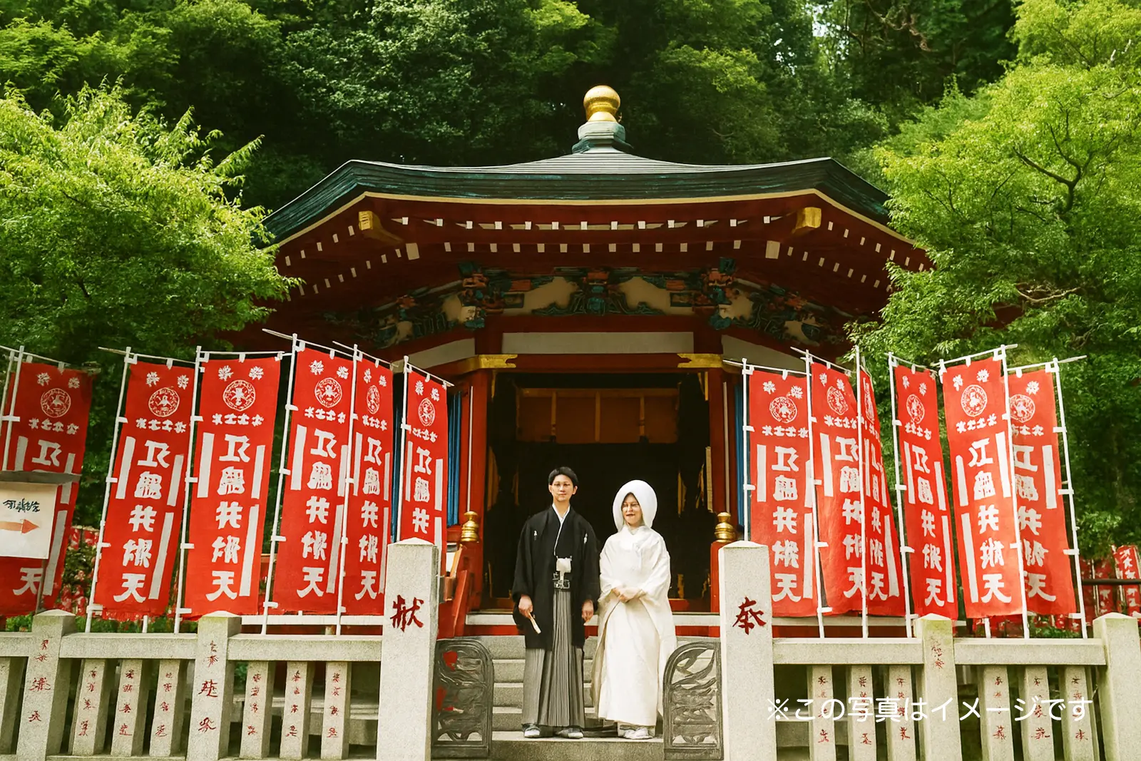 江島神社の境内にて、白無垢姿の花嫁と紋付袴姿の新郎が並ぶフォトウェディング。新緑と赤い旗が美しい、フォトジェリッシュによる本格的な和装前撮り風景。