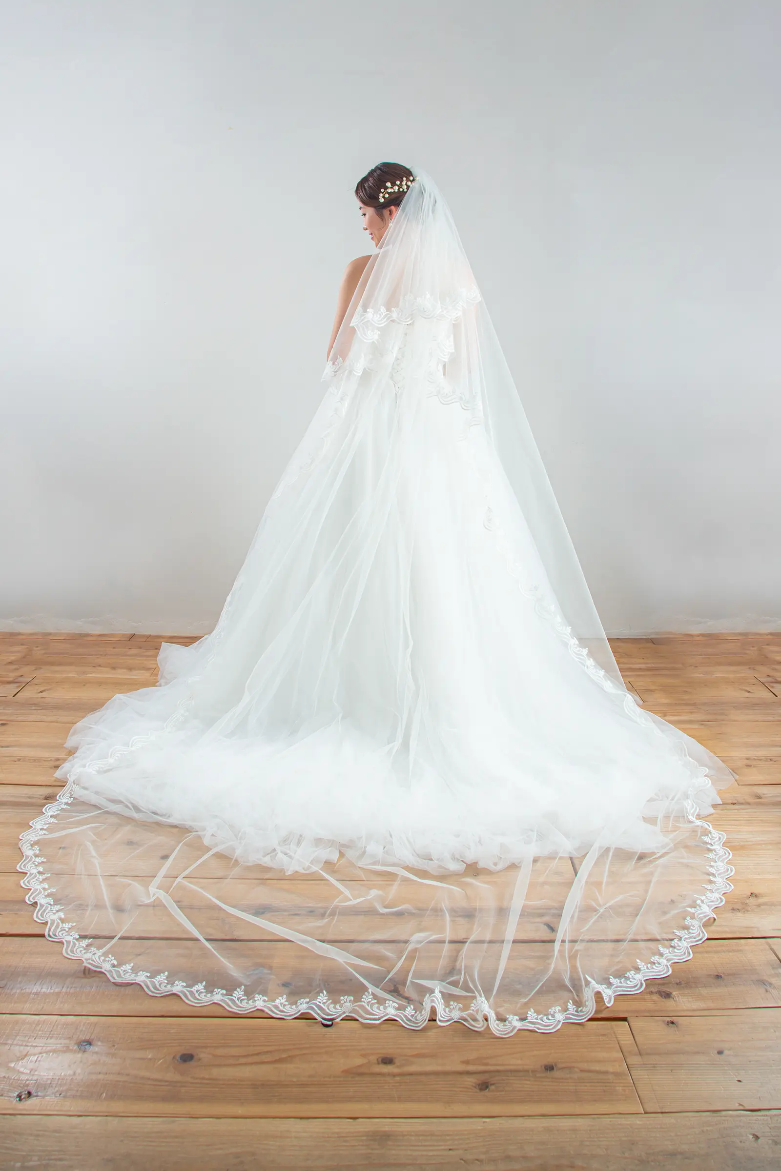 チャペルのバージンロードに美しく広がる、裾に繊細なレースをあしらったロングベールの全身後ろ姿。ウェディングドレスのバックスタイルを引き立てる一枚。