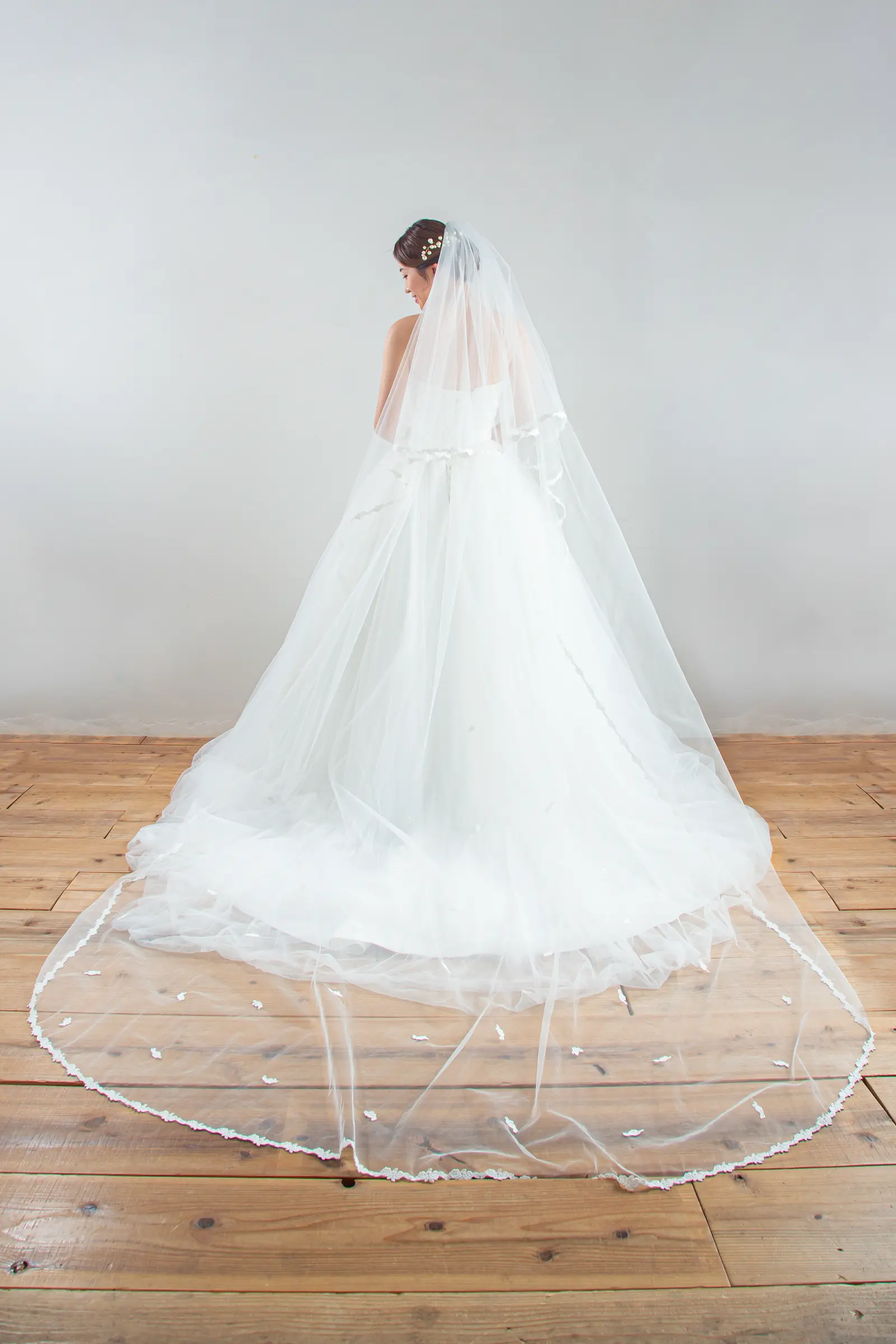 チャペルのバージンロードに美しく広がる、裾に繊細なレースをあしらったロングベールの全身後ろ姿。ウェディングドレスのバックスタイルを引き立てる一枚。