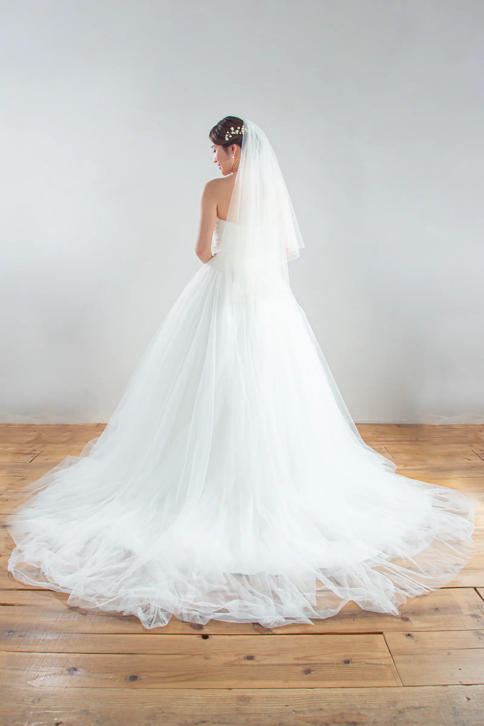 チャペルのバージンロードに美しく広がる、裾に繊細なレースをあしらったミドルサイズのベールの全身後ろ姿。ウェディングドレスのバックスタイルを引き立てる一枚。