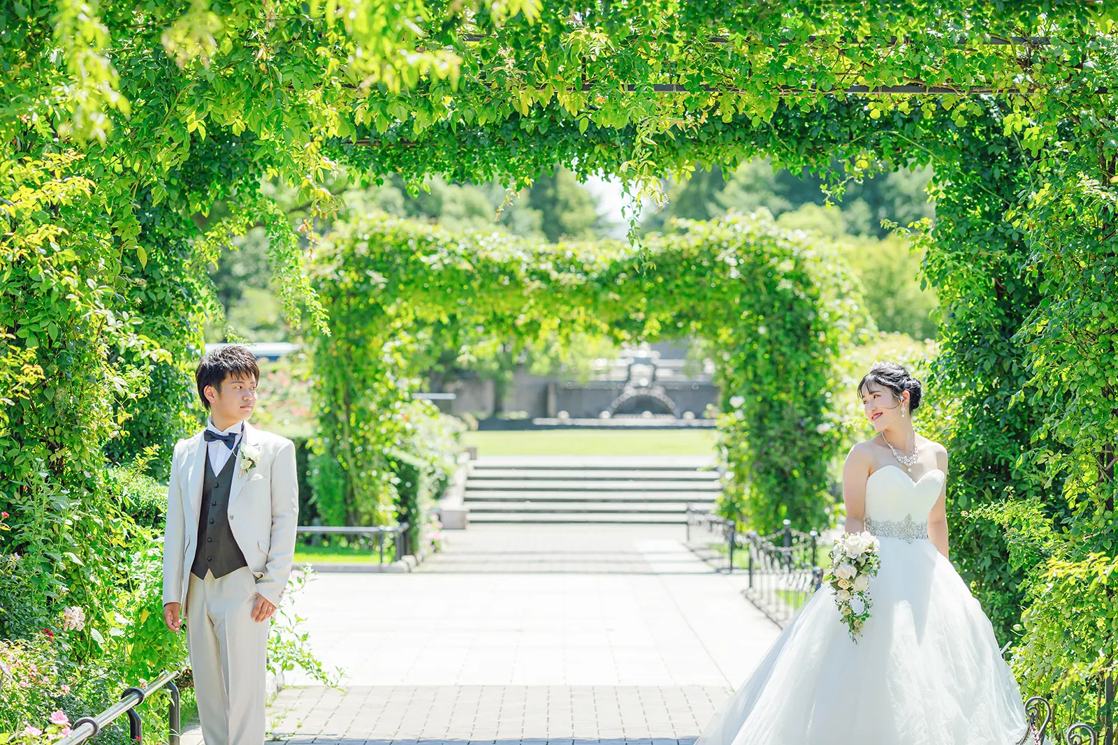 横浜・山下公園の青空と芝生を背景に、ウェディングドレス姿の女性に向かってジャンプするタキシード姿の男性。フォトジェリッシュによる、開放感あふれる楽しいフォトウェディングの一枚。