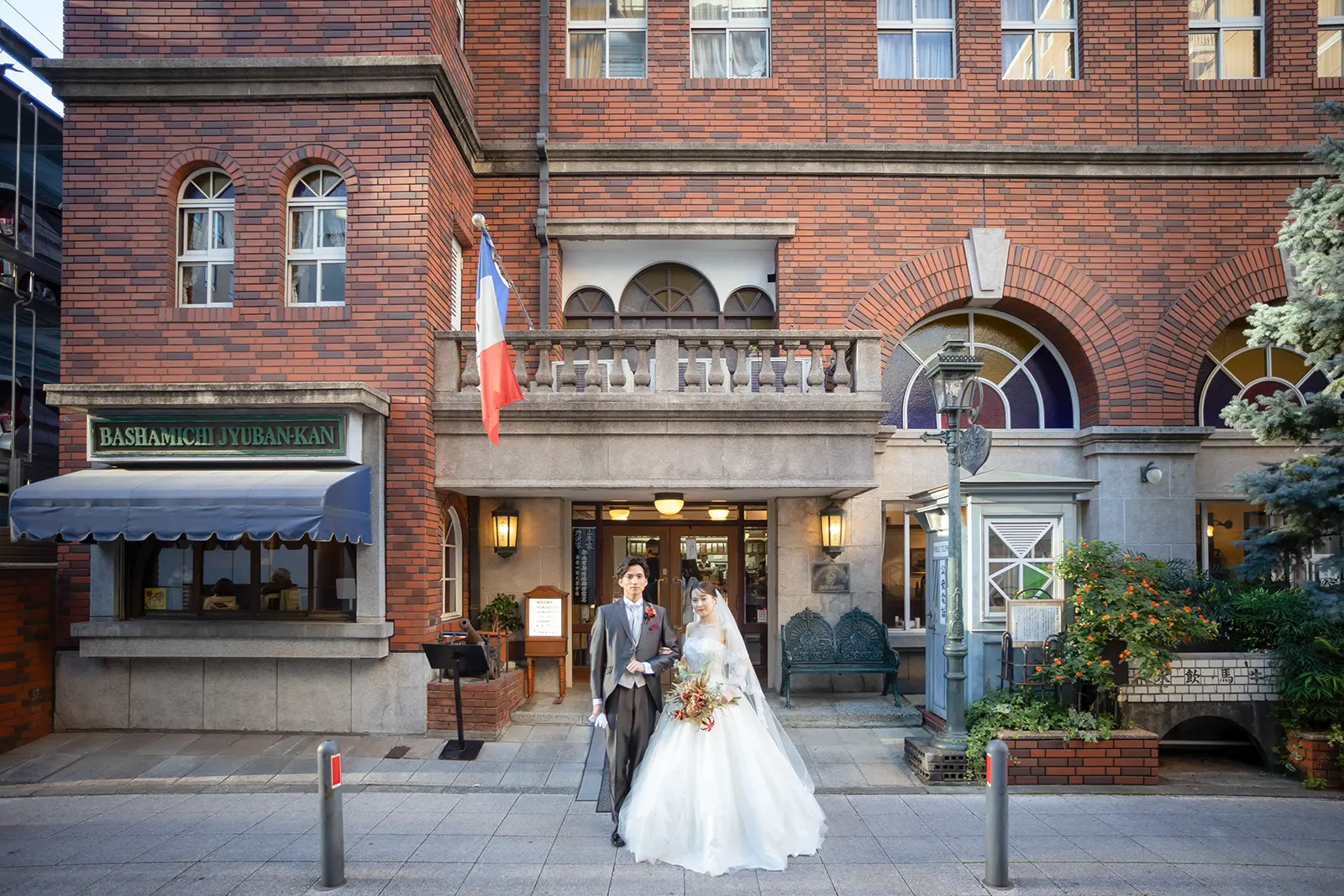 横浜・馬車道十番館のレンガ造りの建物を背景に、ウェディングドレスとタキシード姿の新郎新婦が立つロケーションフォト。レトロでクラシカルな洋館の気品あふれる一枚。
