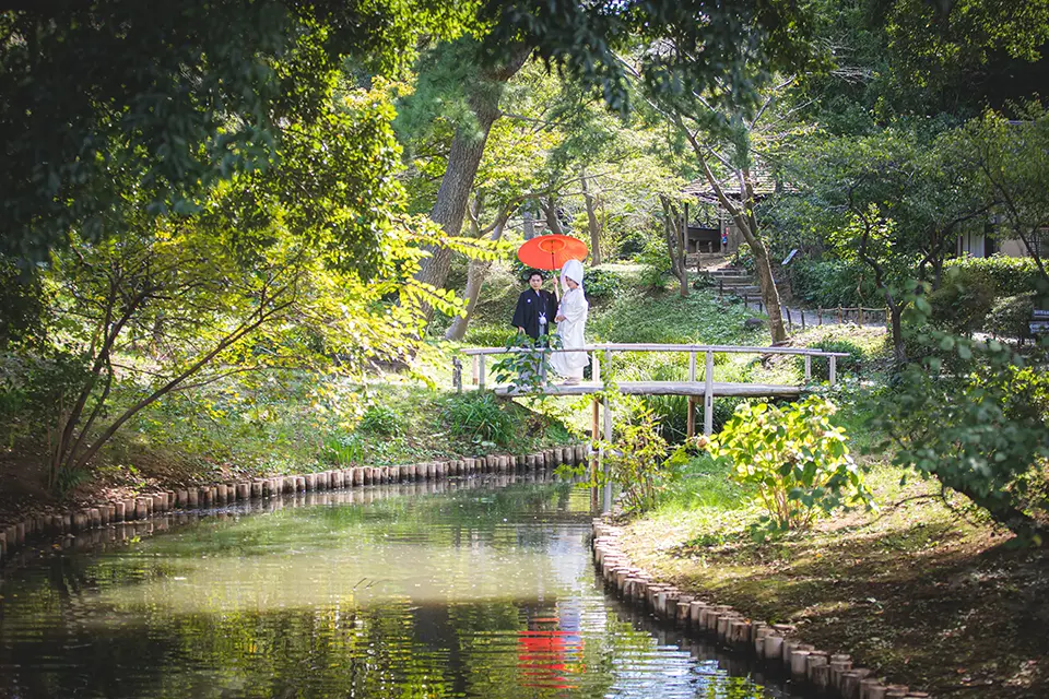 横浜の三溪園で水辺と木々を背景に白無垢前撮りを行う新郎新婦